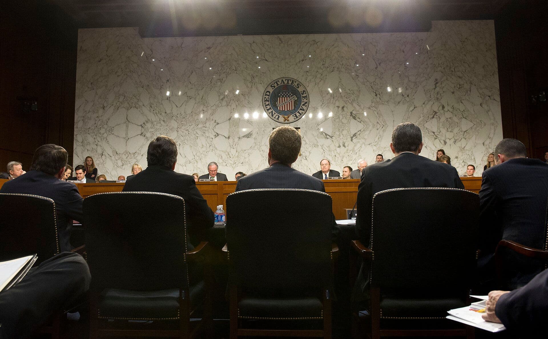 Senate hearing with officials testifying in a formal marble chamber