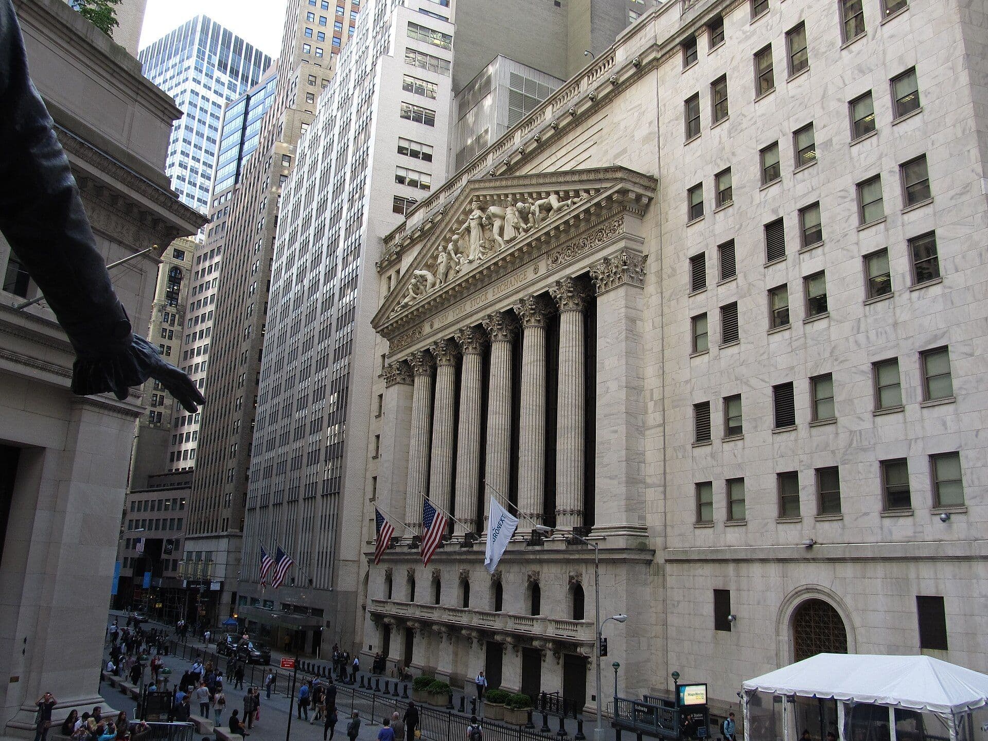 Exterior of the New York Stock Exchange building with classical columns and American flags on Wall Street