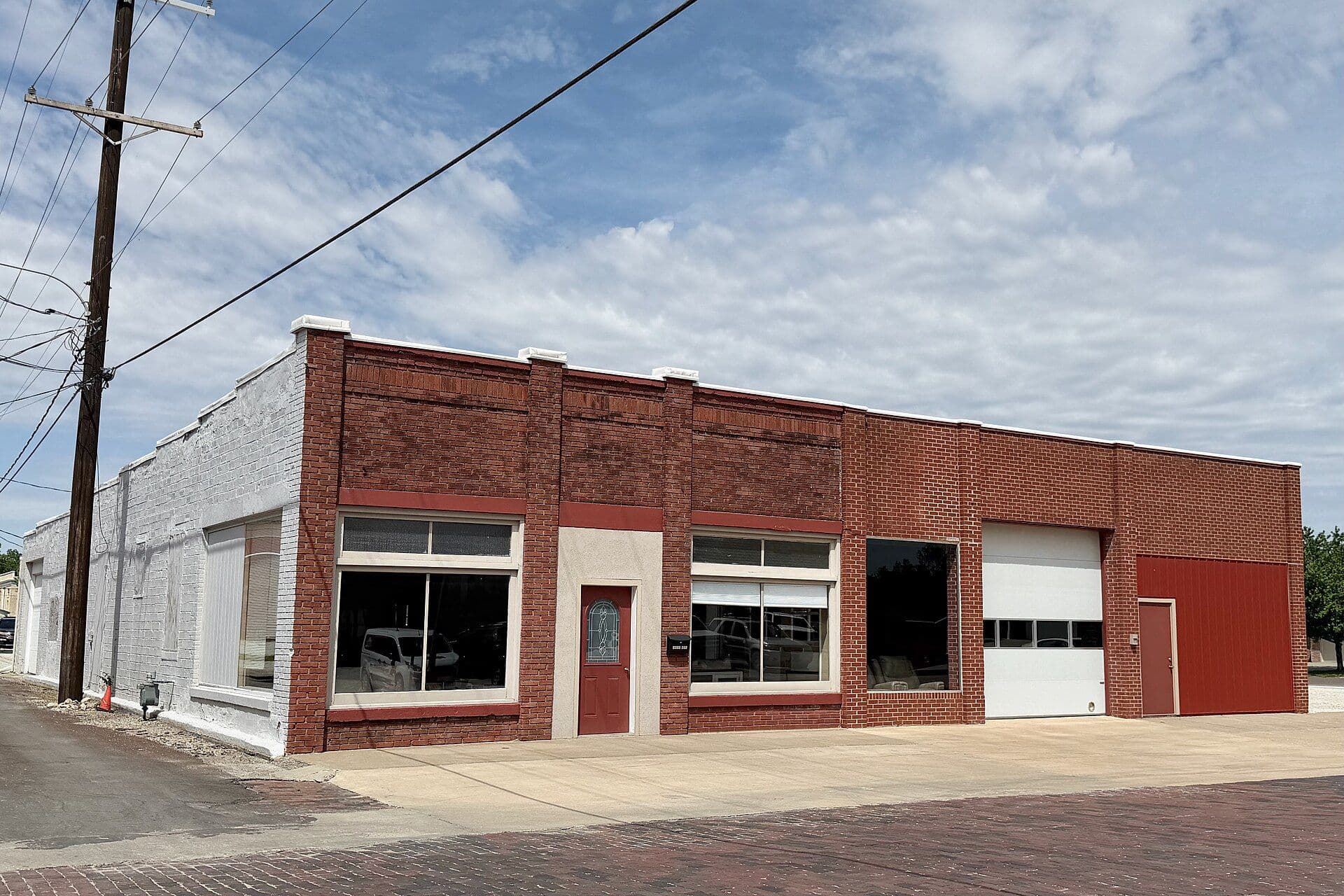 A one-story brick commercial storefront building with a double storefront and garage door under a blue sky