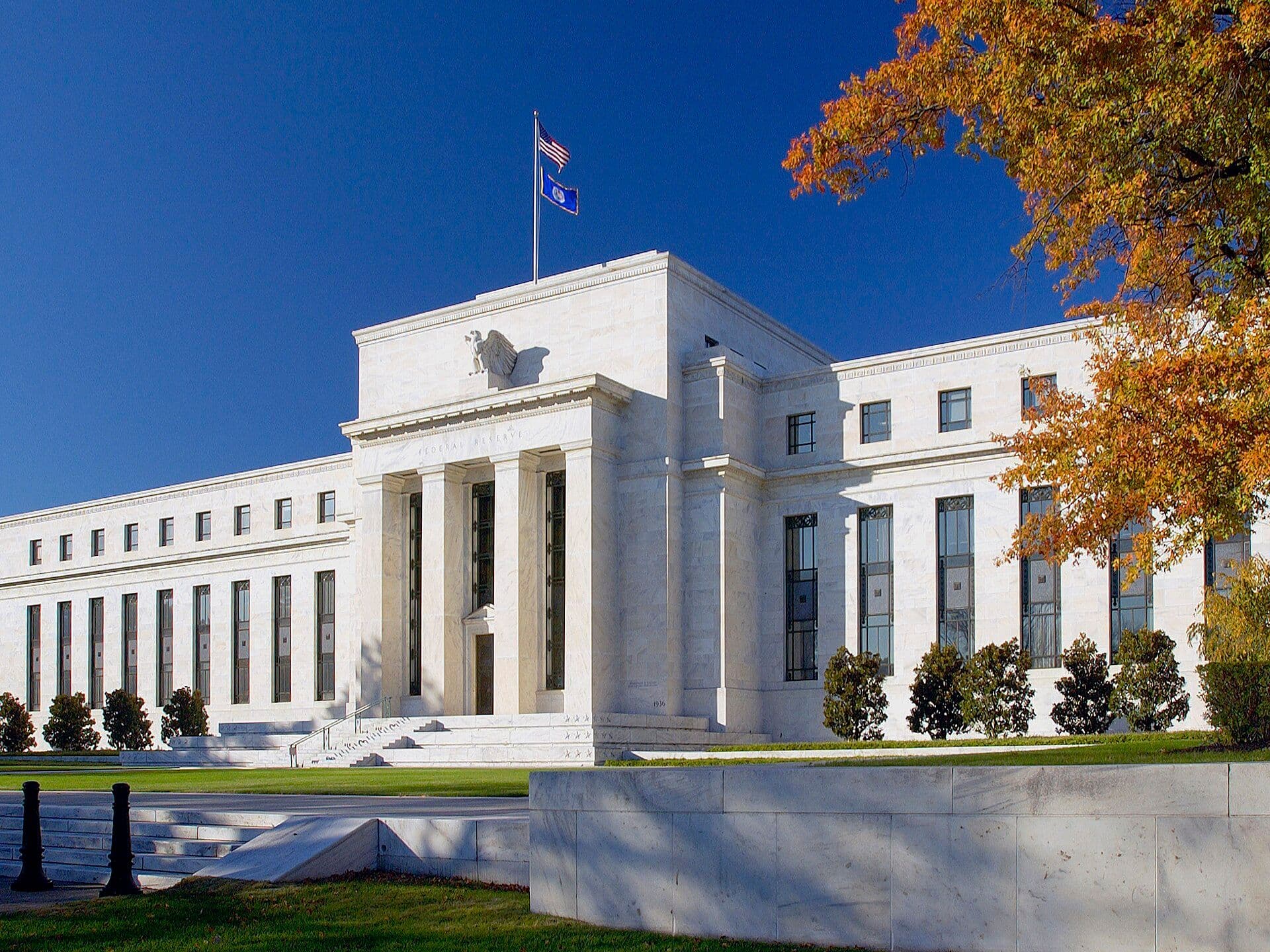 The Marriner S. Eccles Federal Reserve Board building with classical columns and flags, photographed against a clear blue sky