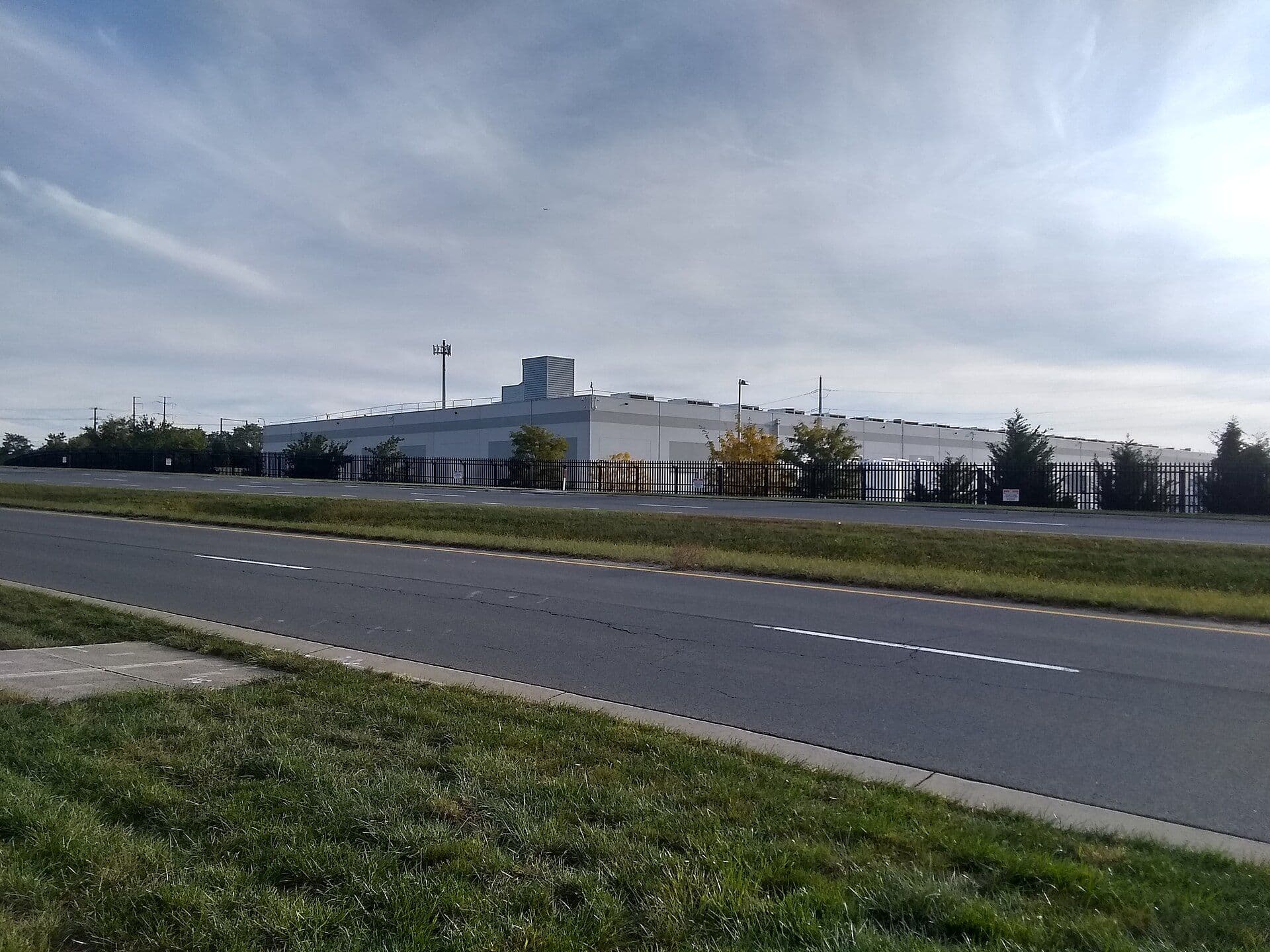 AWS data center facility in Ashburn, Virginia, with security fencing and industrial infrastructure visible against a cloudy sky